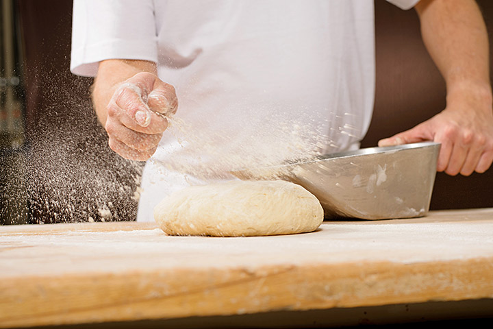 Bäckerhände bestäuben frischen Teig mit Mehl auf dem Holztisch.
