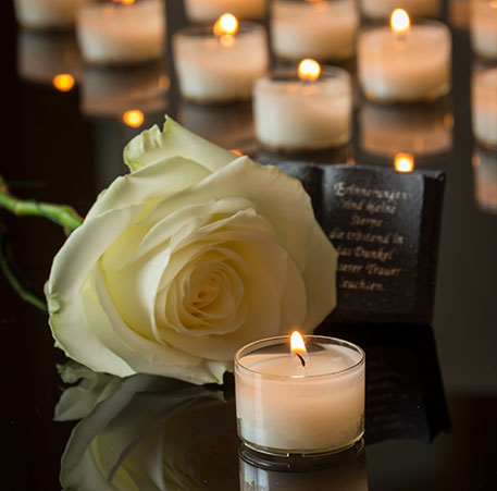Weiße Rose und Kerze an einem Gedenkstein